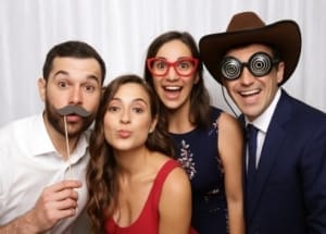 Four wedding guests pose playfully in photo booth with props